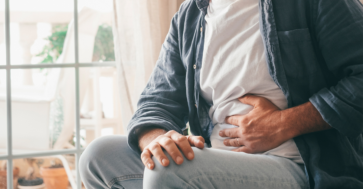 Man suffering with severe stomach pain sitting at home, looking out the window with his hand on his stomach